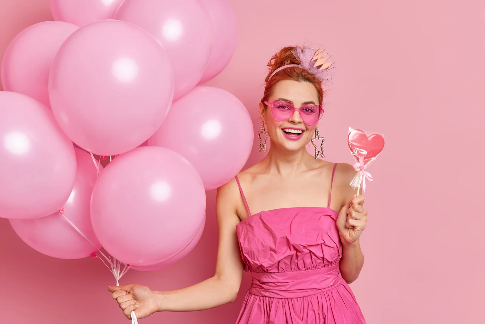 Jeune femme tenant des ballons roses et portant des lunettes roses en forme de cœur, faisant un sourire à son enterrement de vie de jeune fille avec leonardo animation.